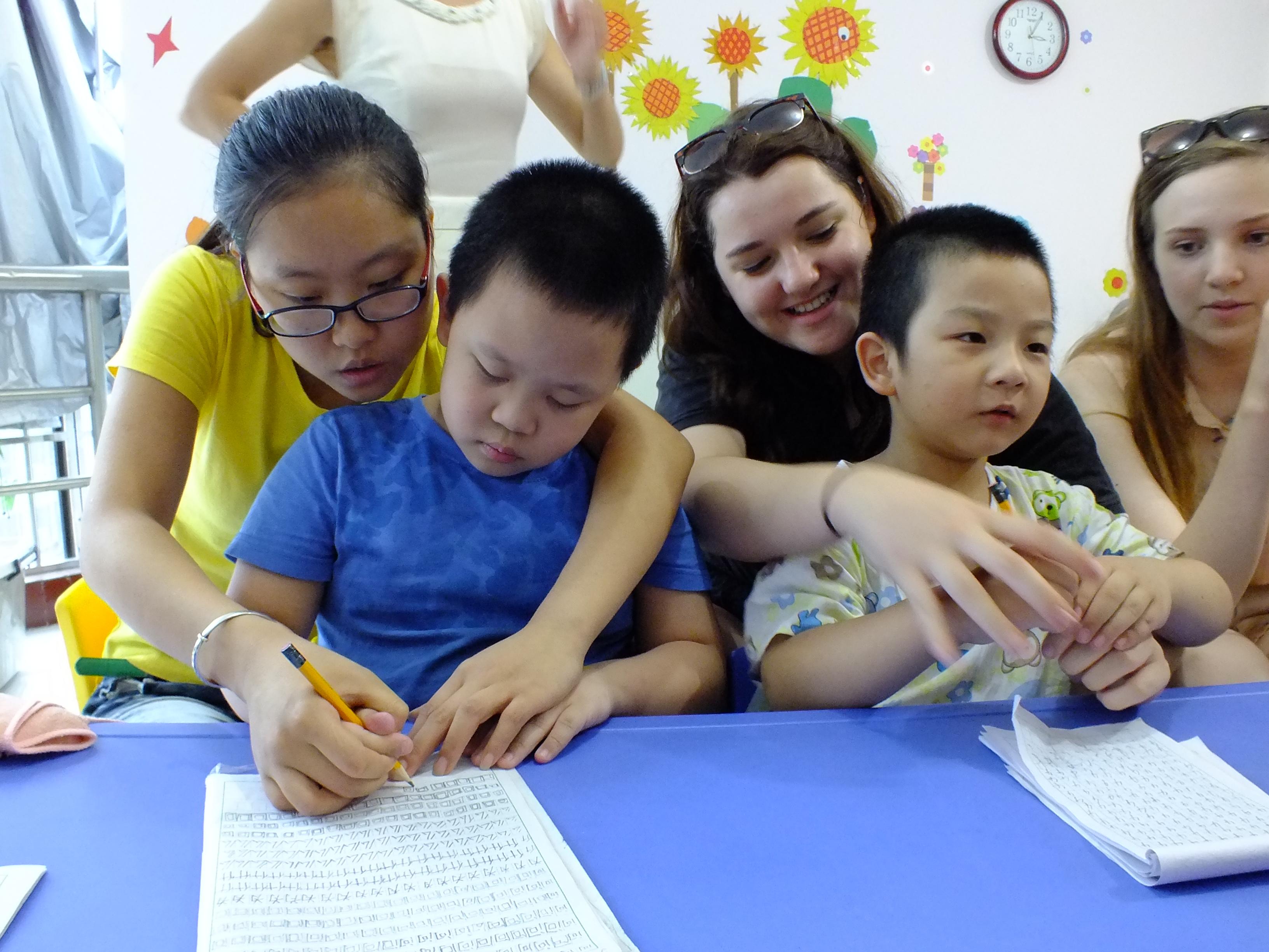 Female Projects Abroad volunteers help children develop their literacy skills at a Childcare Project in China. Two female Childcare volunteers working with kids in China help two young boys practice writing in English at a kindergarten.